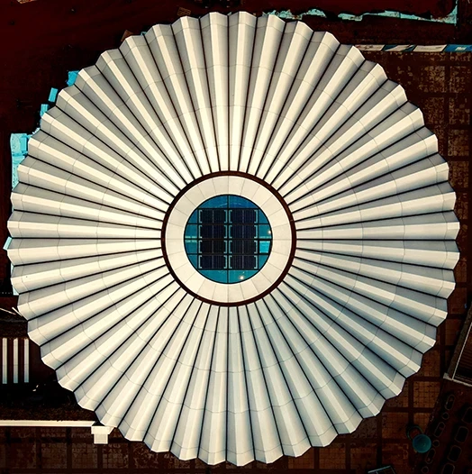 Symetryczny dach budynku w kształcie kopuły sfotografowany z lotu ptaka, z promieniście ułożonymi panelami