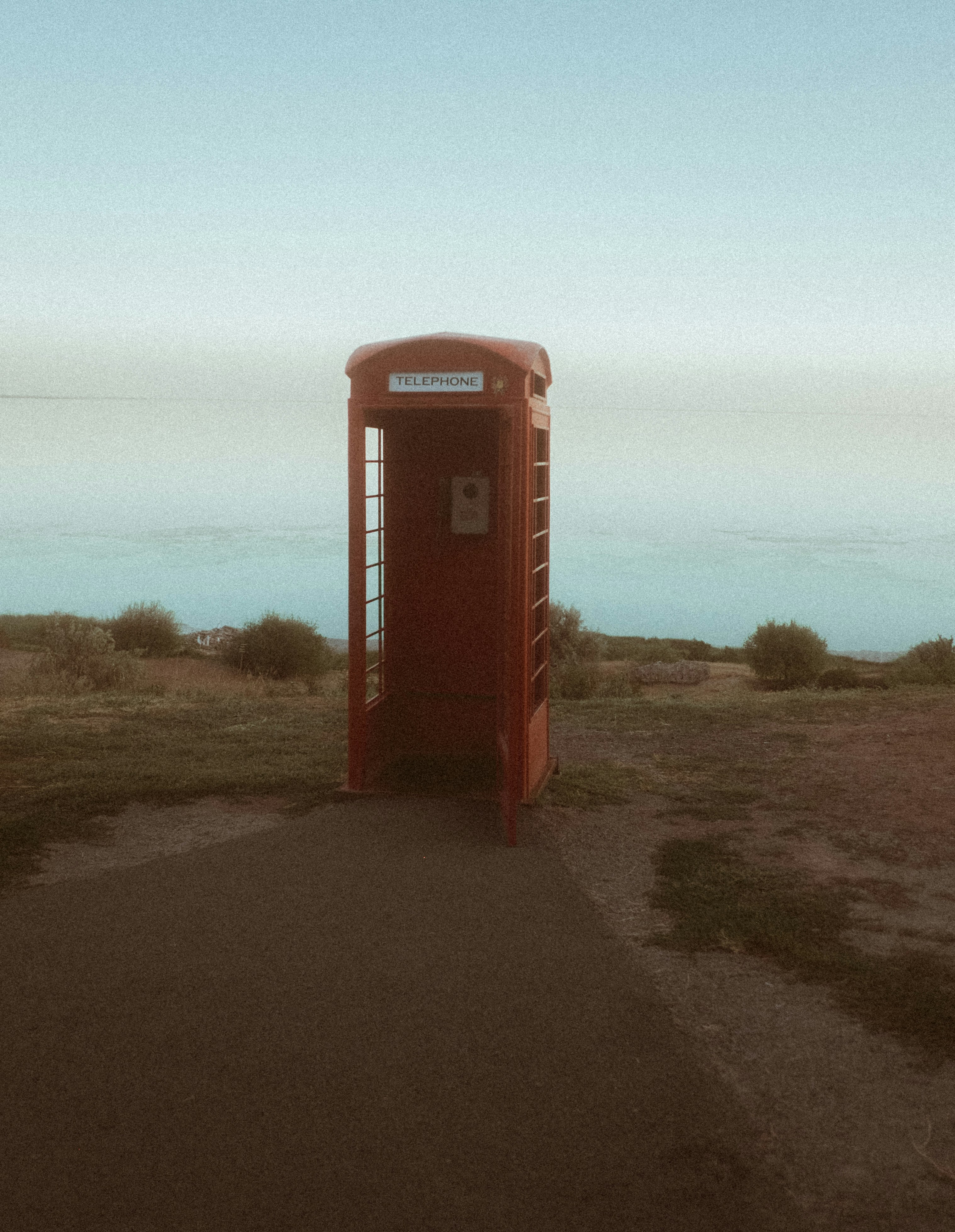 Red telephone booth on a grassy cliff overlooking the ocean.