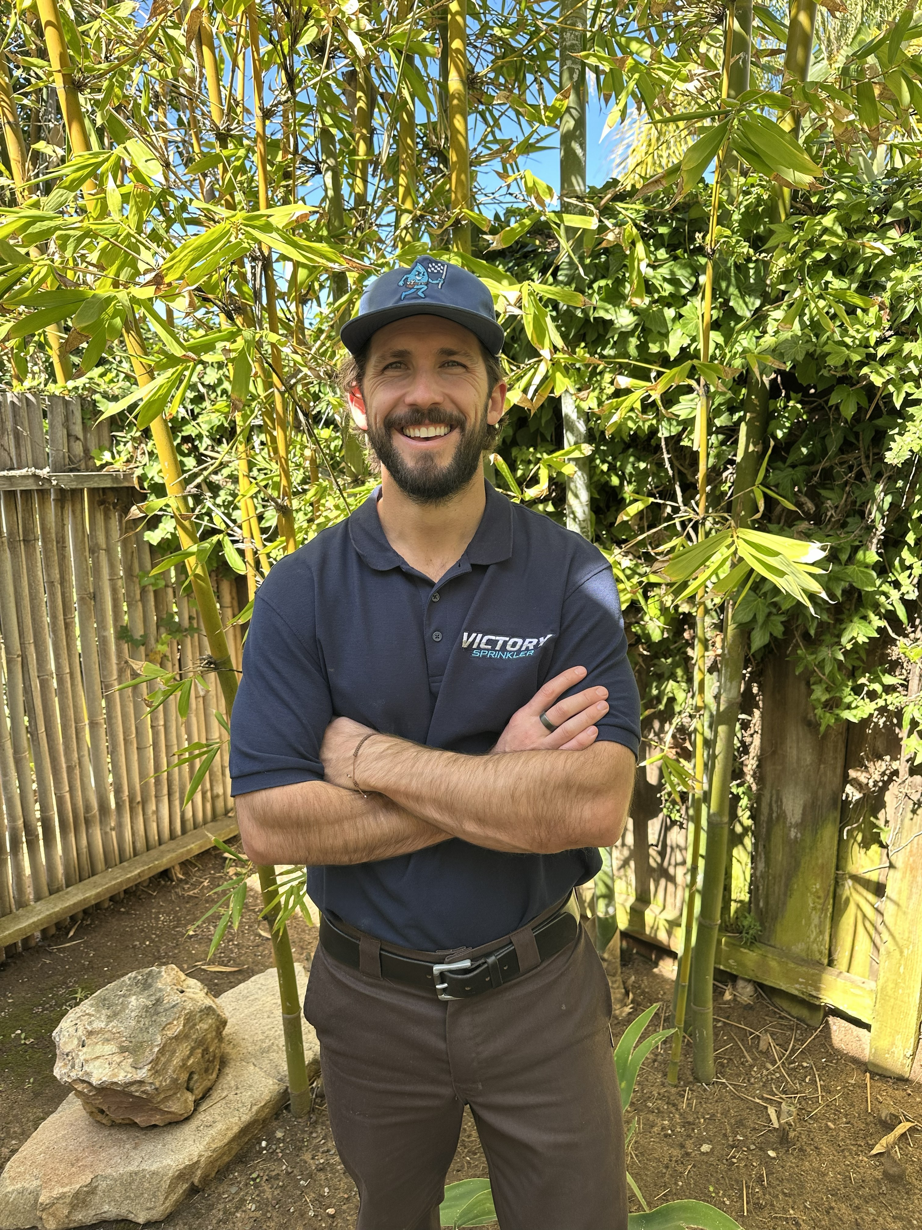 Christian, owner of Victory Sprinkler, smiling in a lush backyard filled with tropical plants after a professional irrigation repair and service.