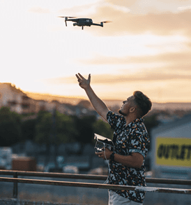 A man in a brown suit and cream silk scarf poses against a neutral background, exuding a composed and sophisticated demeanor.