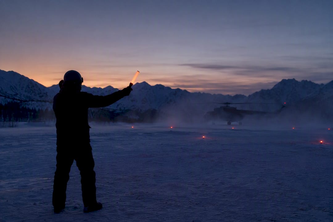Ground marshaller signalling near a helicopter at dusk