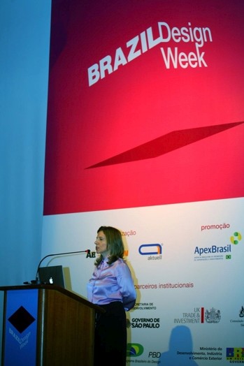 A photo o a woman at a stand giving a lecture and behind her a poster with text: Brazil Design Week.