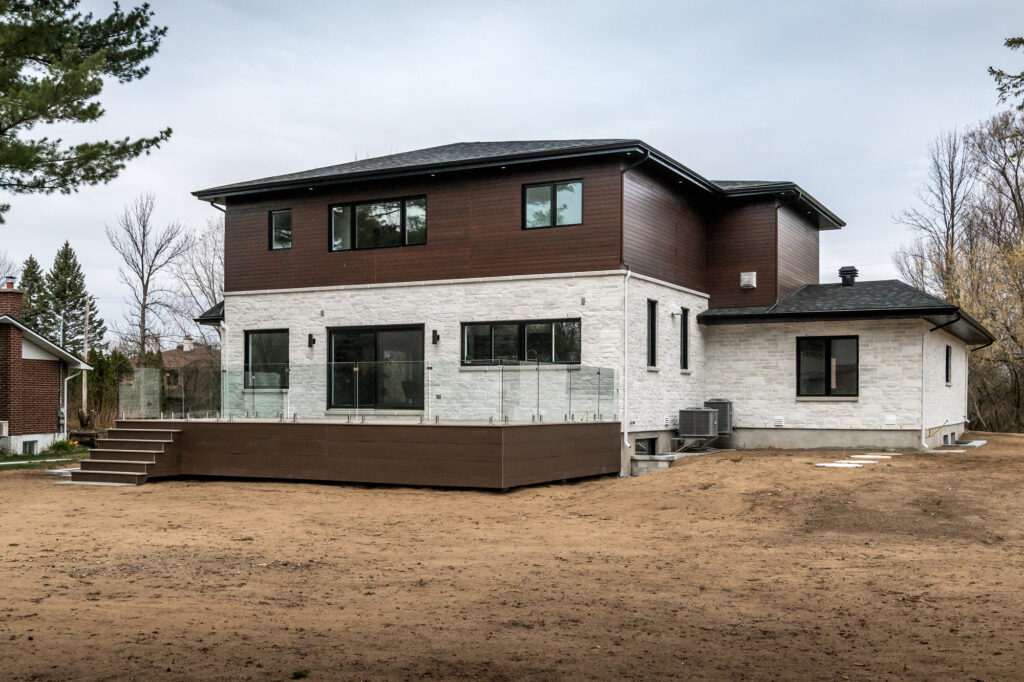 Modern two‑storey home with dark upper and light stone‑clad lower exterior, paved front walkway and large windows showcasing the high‑end residential properties serviced by B&Y Reno Corp