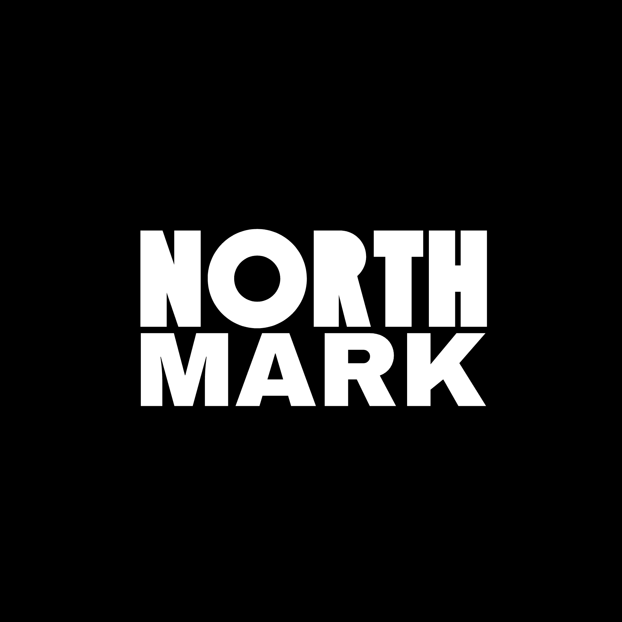 A man with wavy brown hair smiles slightly while wearing a black turtleneck and blazer. The background is softly blurred, suggesting a sunny outdoor setting.