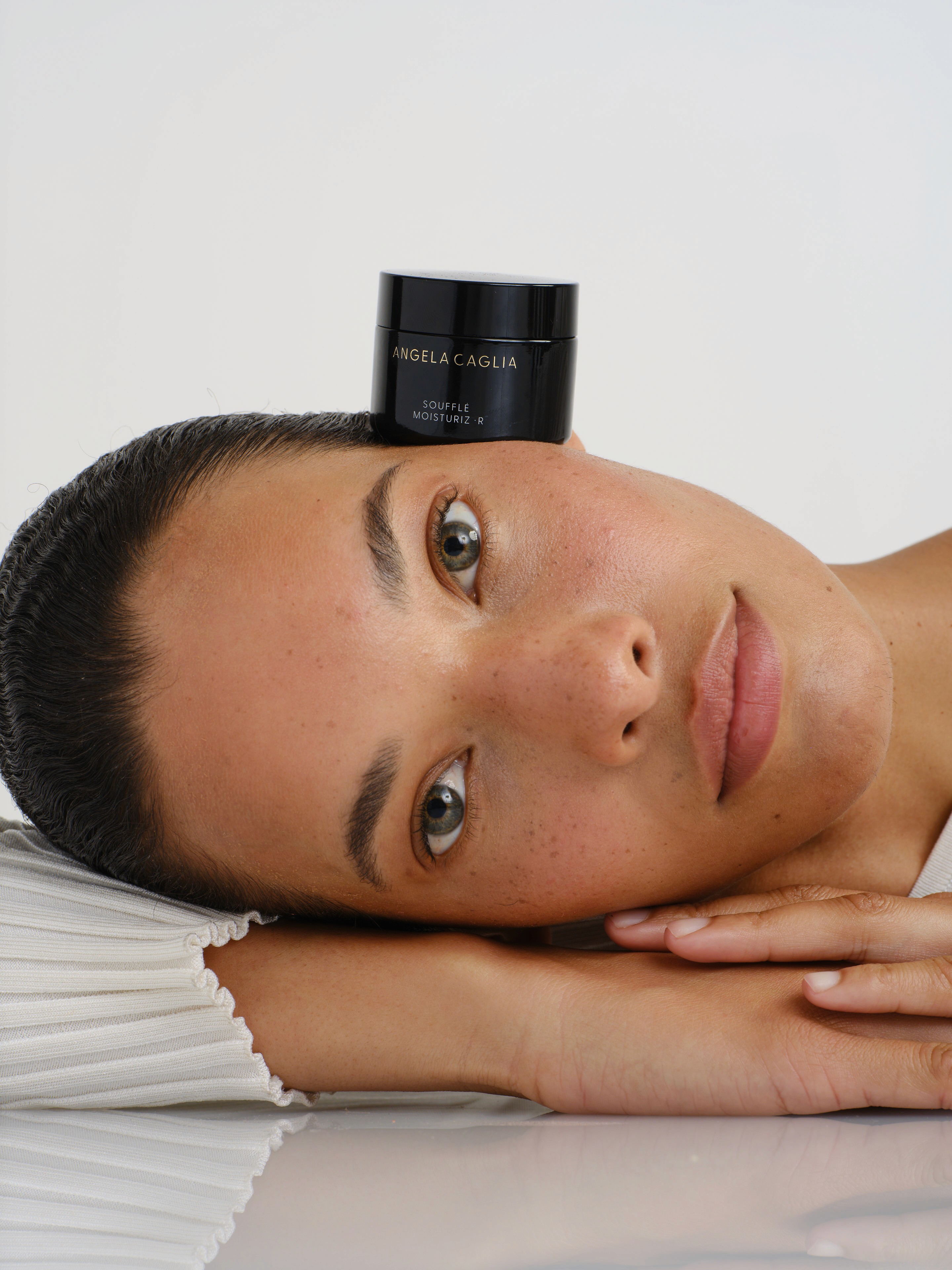 Woman resting head down, skincare jar balanced near her temple