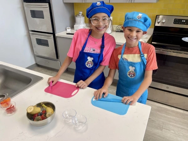 Two young chefs about to prepare food, smiling at the camera.