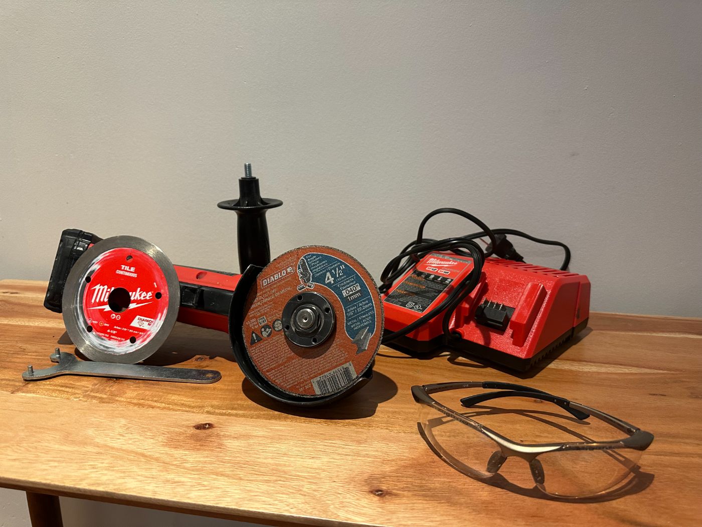 Meuleuse sans fil Milwaukee avec disques de coupe, chargeur, clé de serrage et lunettes de protection sur table en bois