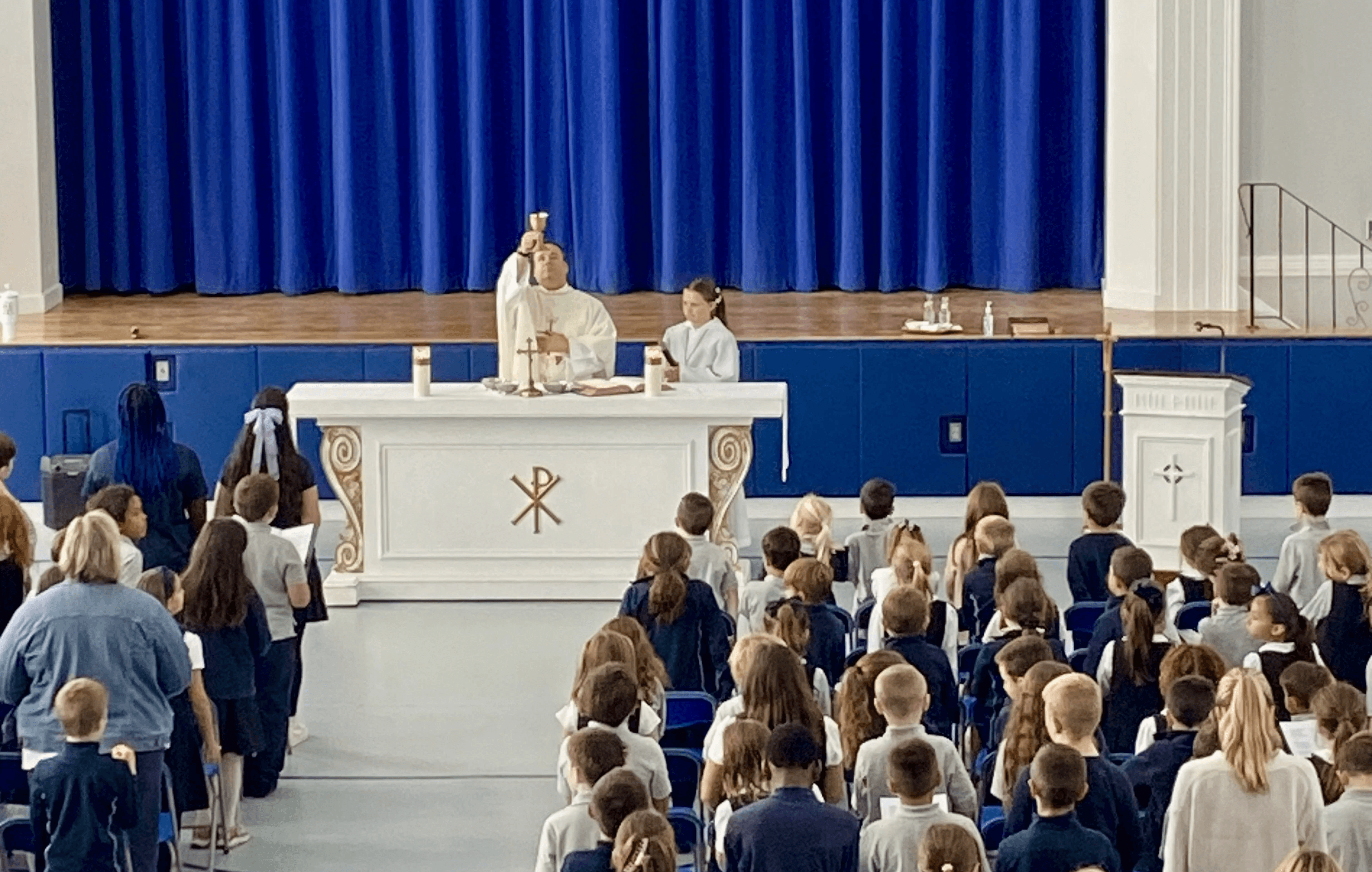 A priest elevating the chalice during school Mass in the gym
