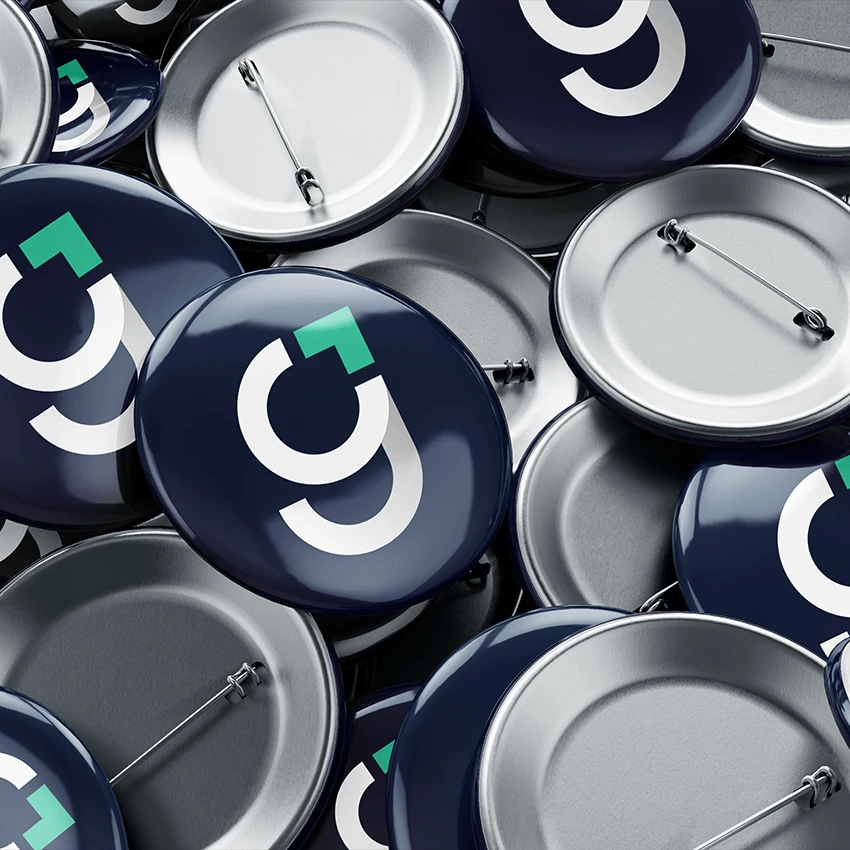 A pile of glossy navy pin badges printed with the white "g" monogram and mint corner mark, mixed with badges turned over to show their silver backs and pins.