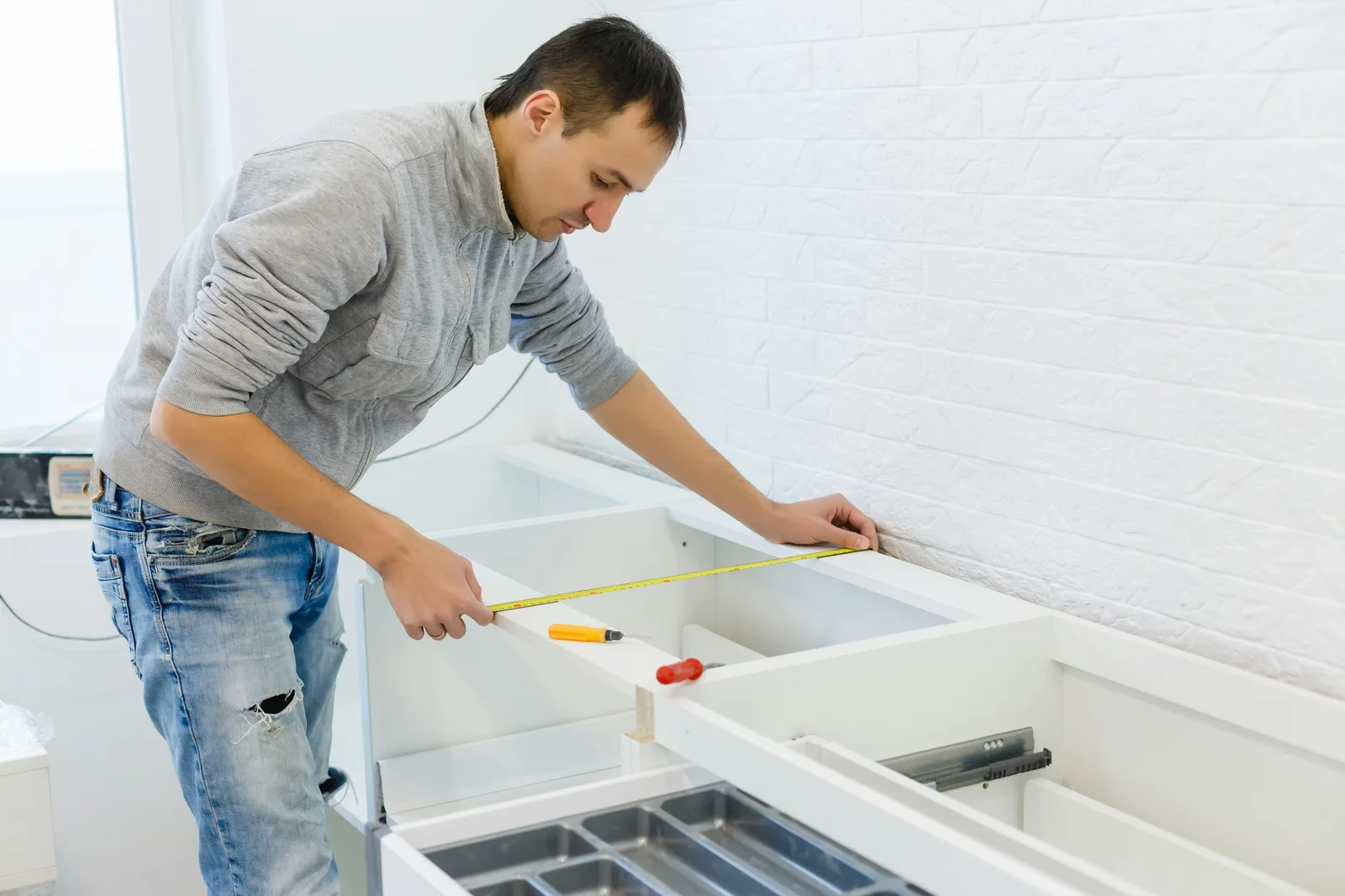 Man measuring white kitchen cabinet drawers with tape measure