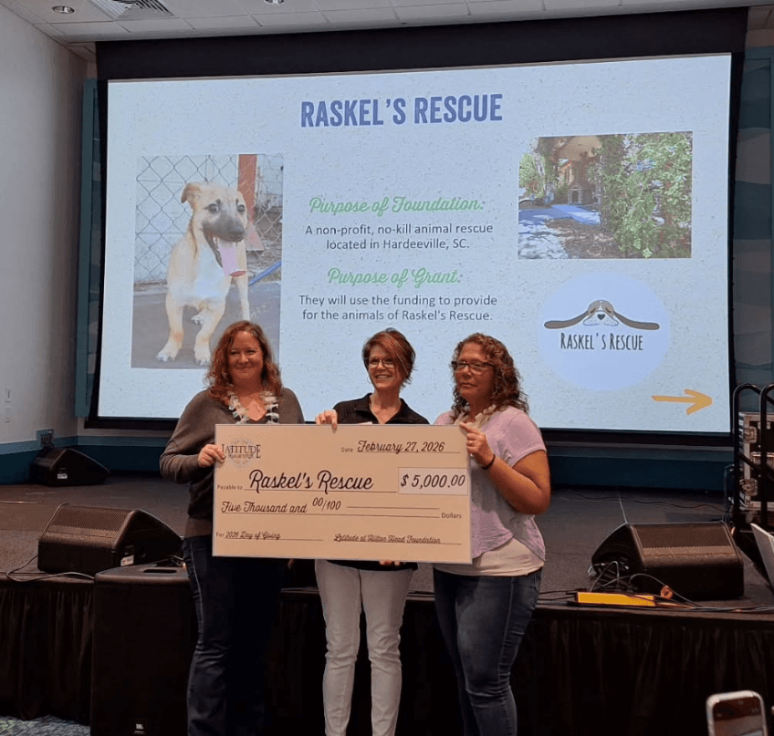 Three individuals hold a large check in front of a presentation screen with maps and information displayed.