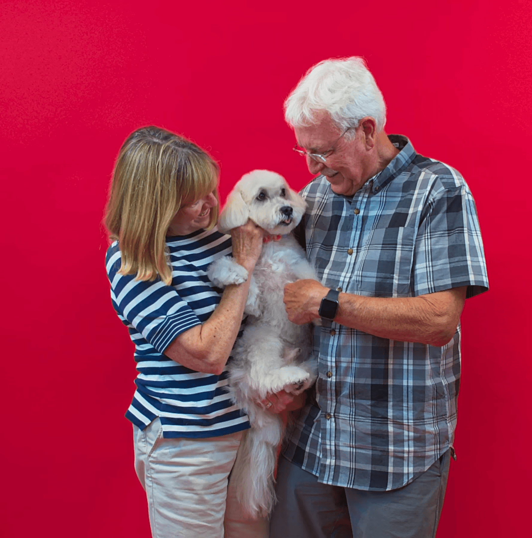 Older couple smiling while holding their small white dog to show affection, loyalty, and happiness after grooming.