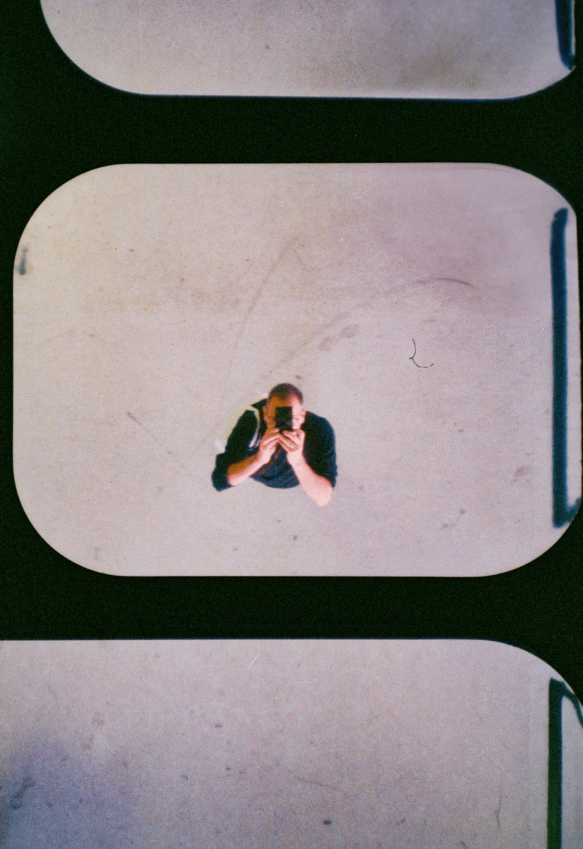 Top-down view of a person holding a camera and taking a photo, framed within a film-style border.