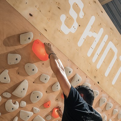 Indoor Bouldern an der Shiny Wall Systemwand – Kletterer greift farbige Griffe an einer interaktiven Boulderwand mit über 2.000 Routen. Urbanes Bouldern in München.