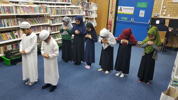 Pupils praying together in the library, sitting in rows on the carpet between the bookshelves.