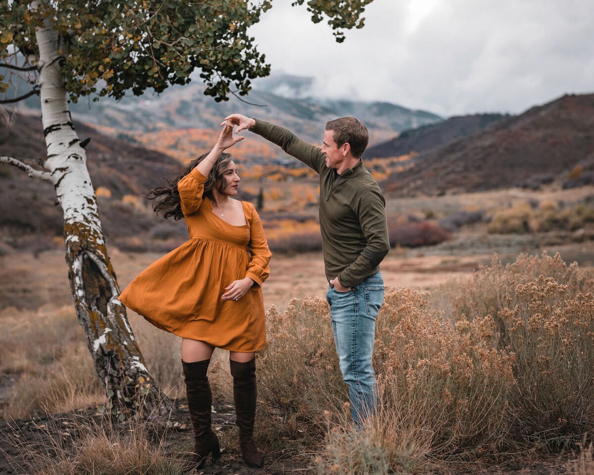Couple twirling in a Snowmass meadow with mountains behind them.