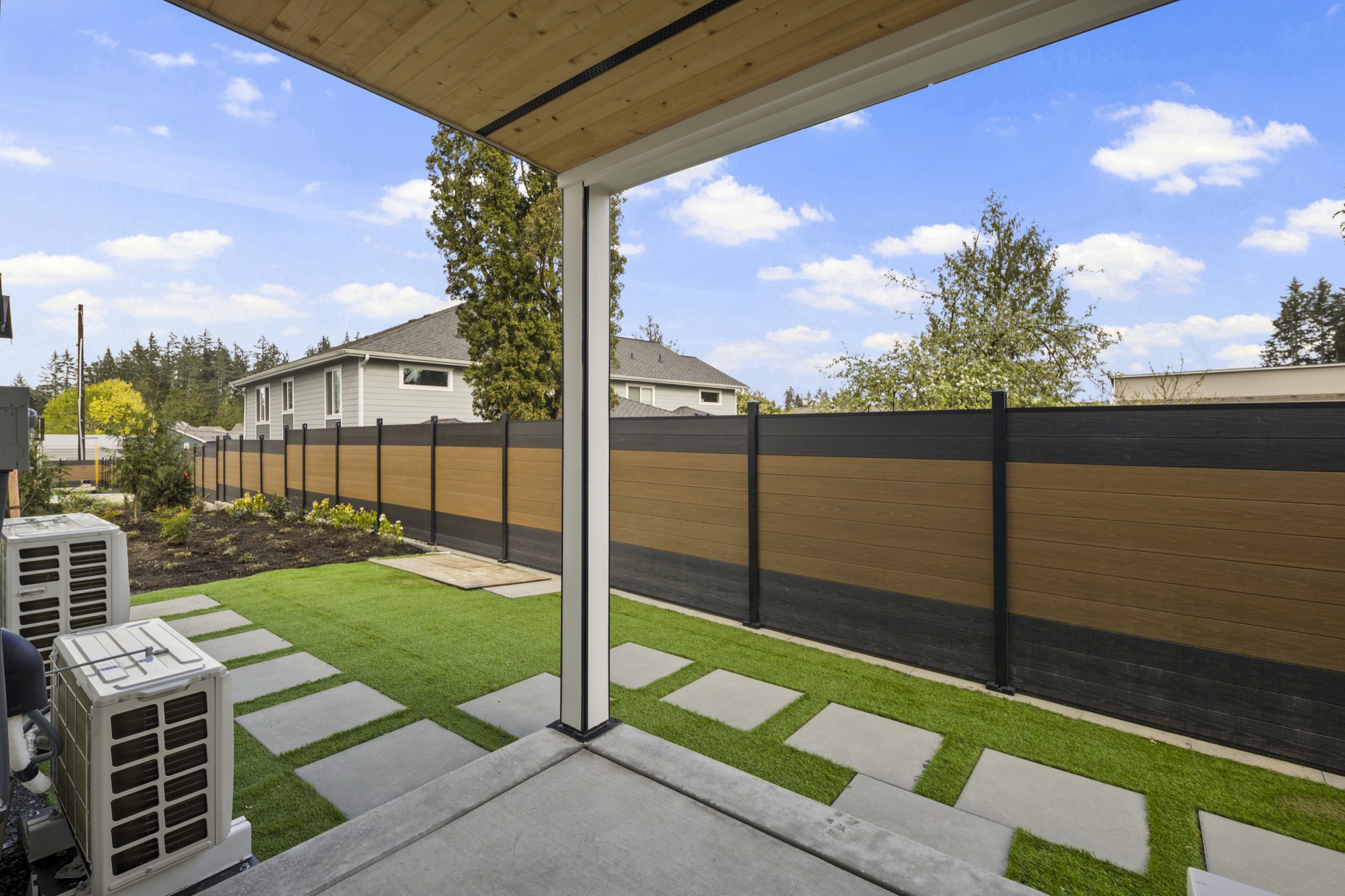 Private outdoor patio of a luxury home with artificial turf lawn, stepping stone path, wood privacy fence, and covered pergola with HVAC unit