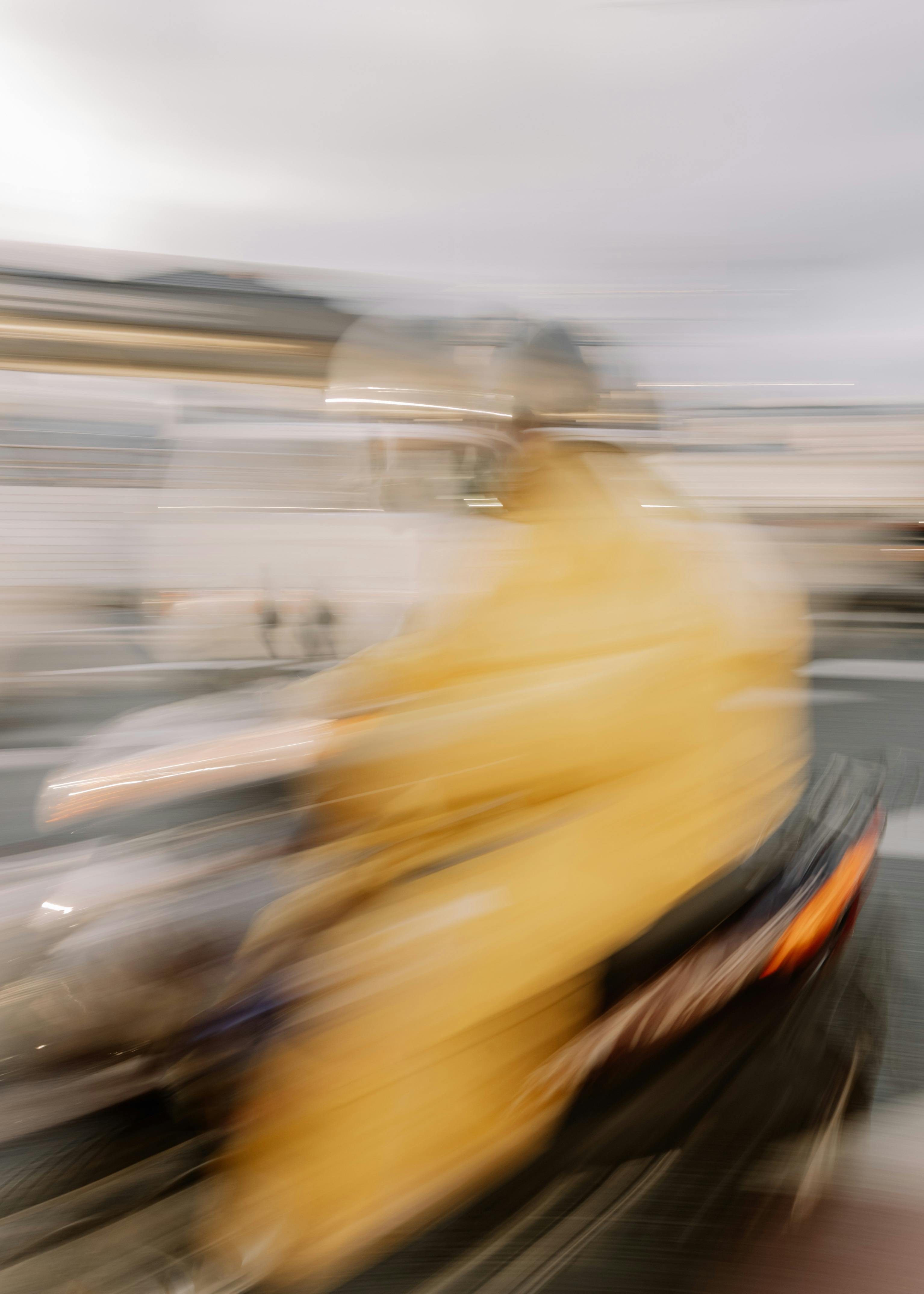 Close-up portrait of a person wearing a gray insulated hooded jacket with the hood up, showing their face framed by the hood against a light background.