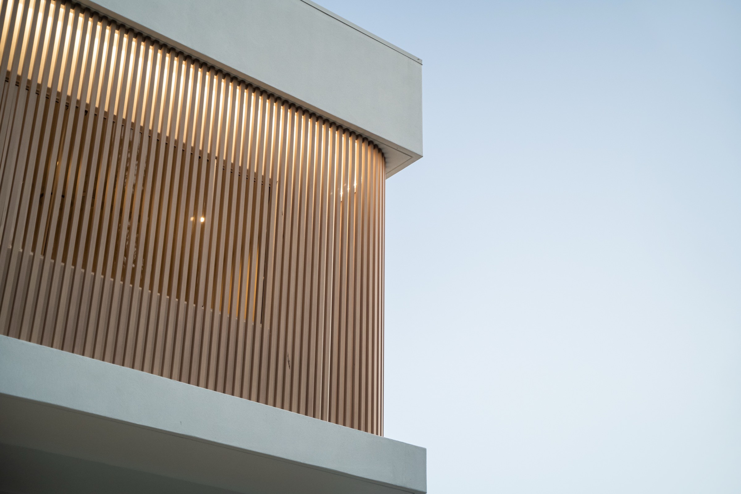 Detail of Casa Palmera's timber-batten facade against open evening sky