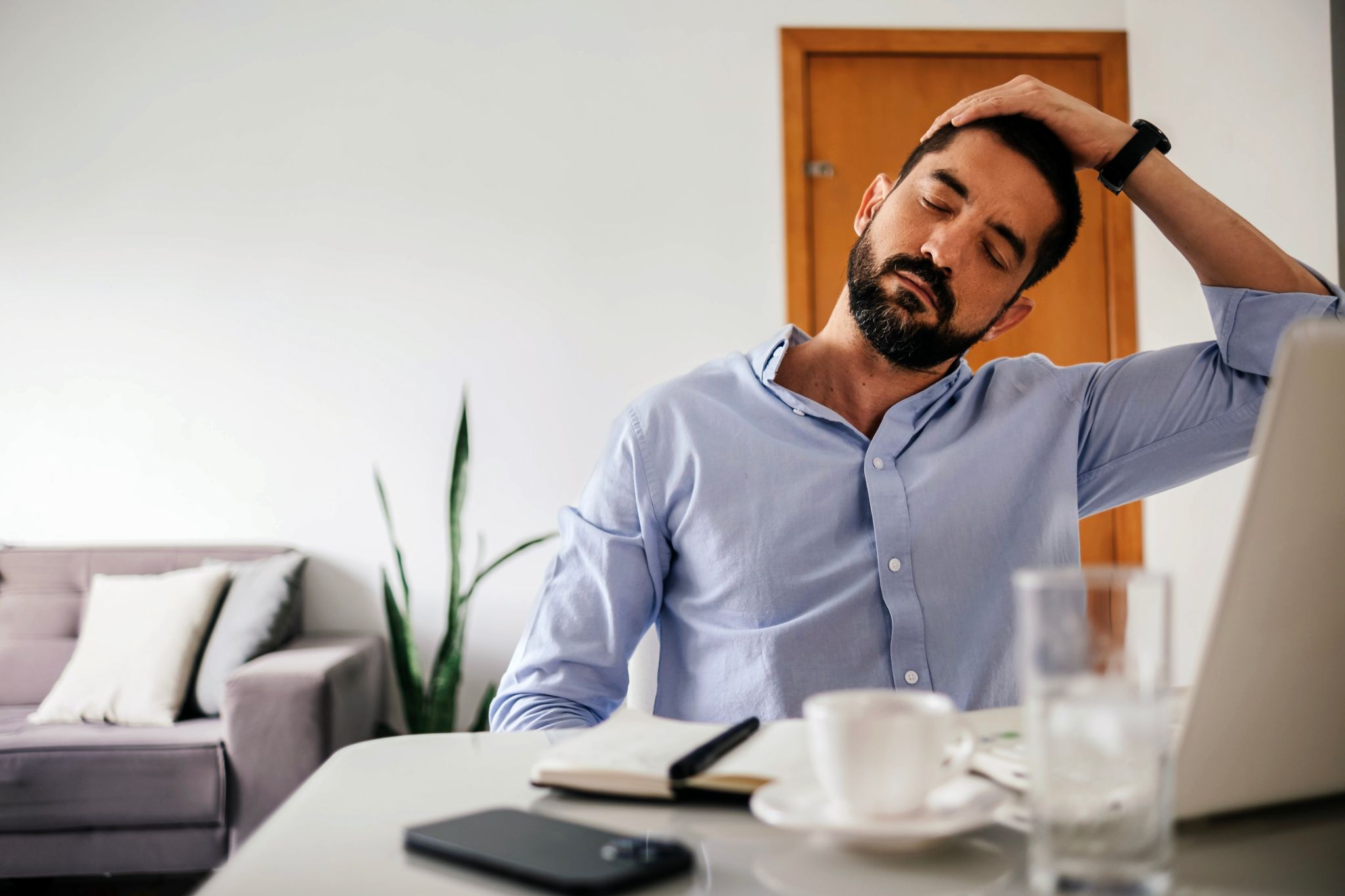 Man sitting at a desk gently stretching his neck to relieve tension while working.