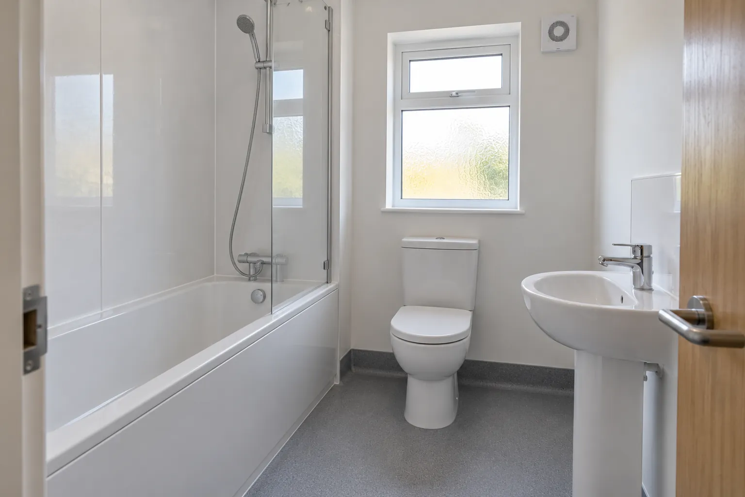Newly replaced social housing bathroom with white bath and shower screen, white wall panels, toilet, basin and extractor fan