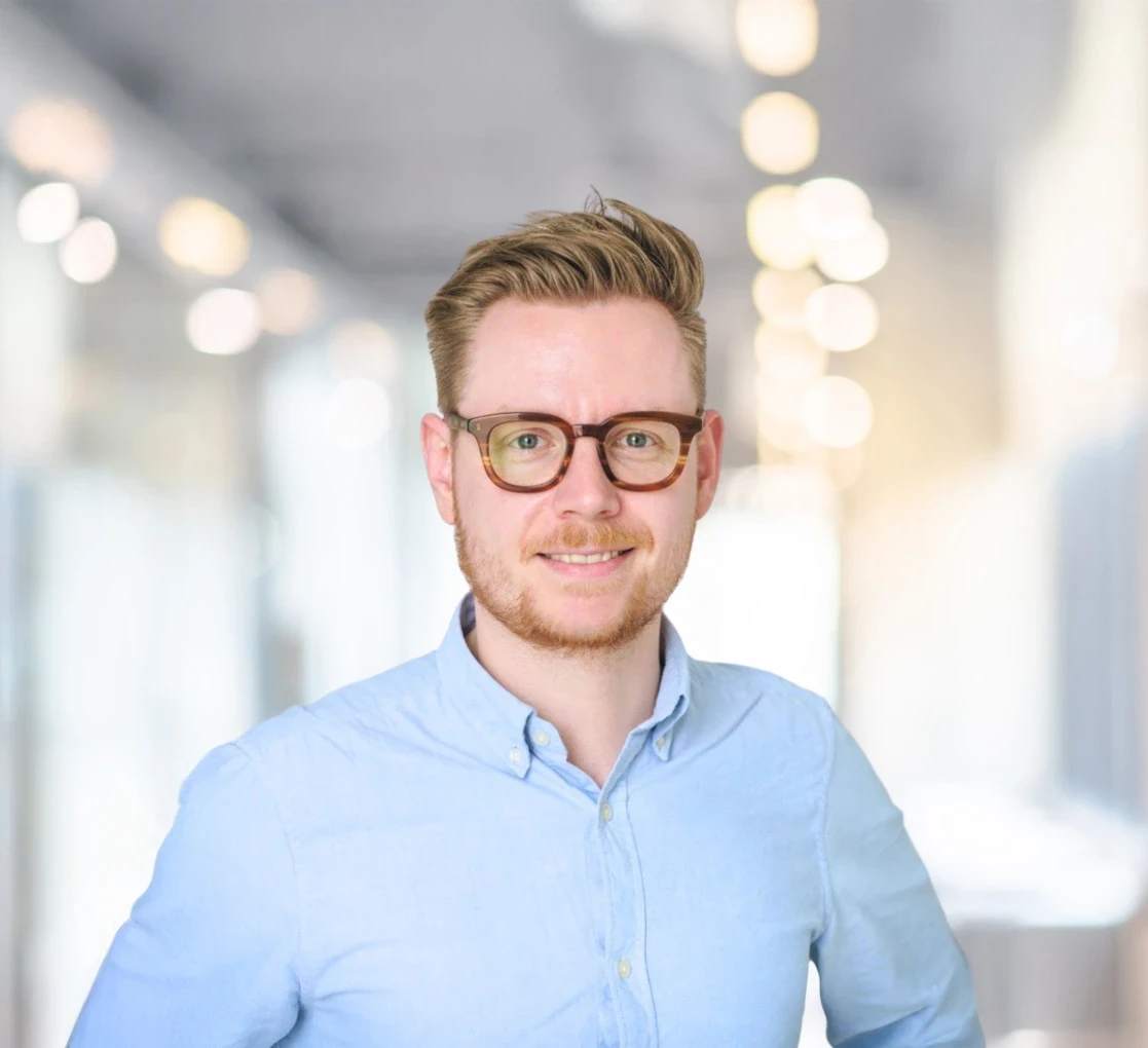Dennis Meyer Philippi, Geschäftsführer von Tantum Sana, Portrait eines Mannes mit Brille im hellblauen Hemd vor modernem Bürohintergrund.
