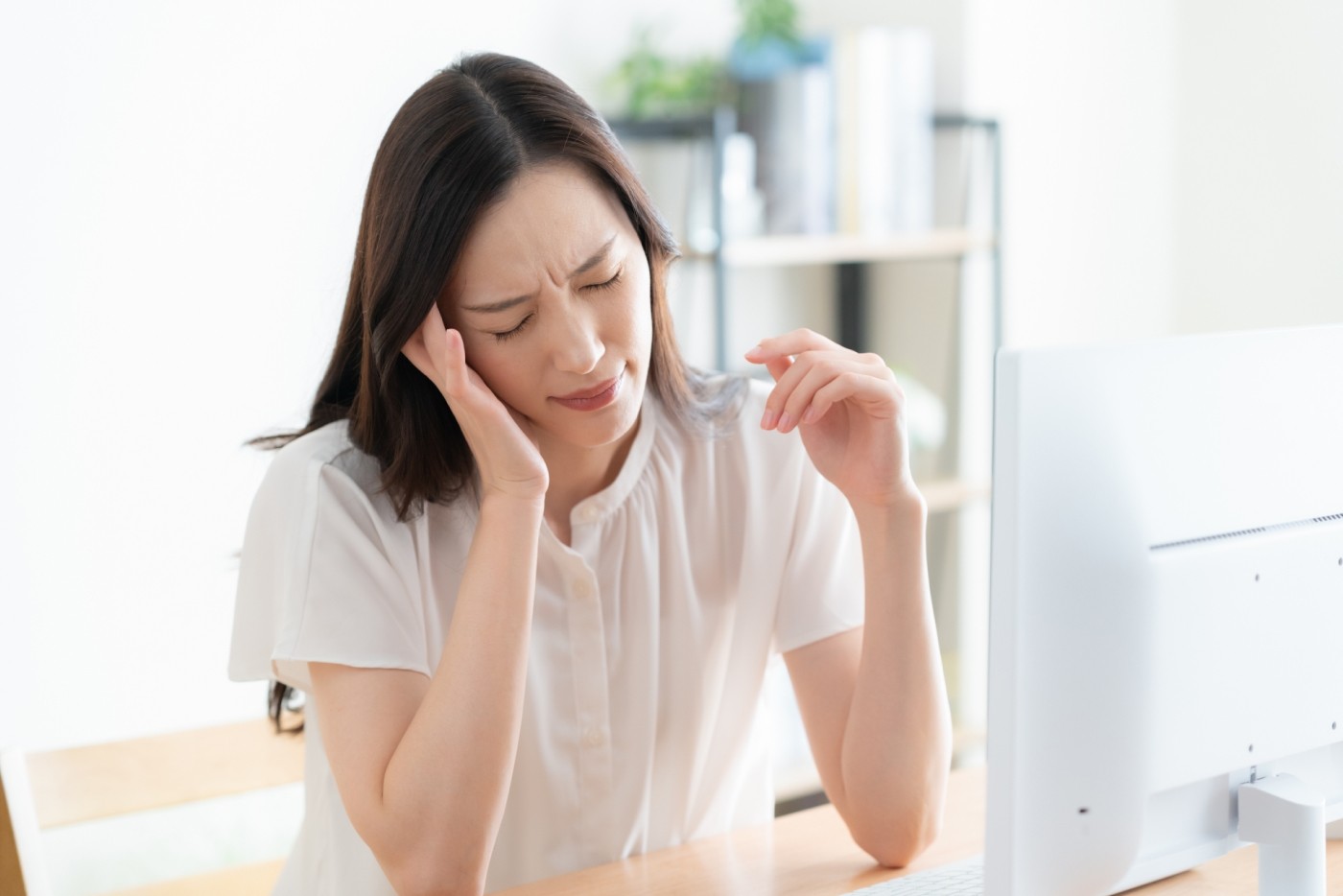 パソコンの前でこめかみを押さえて苦しそうにする女性
