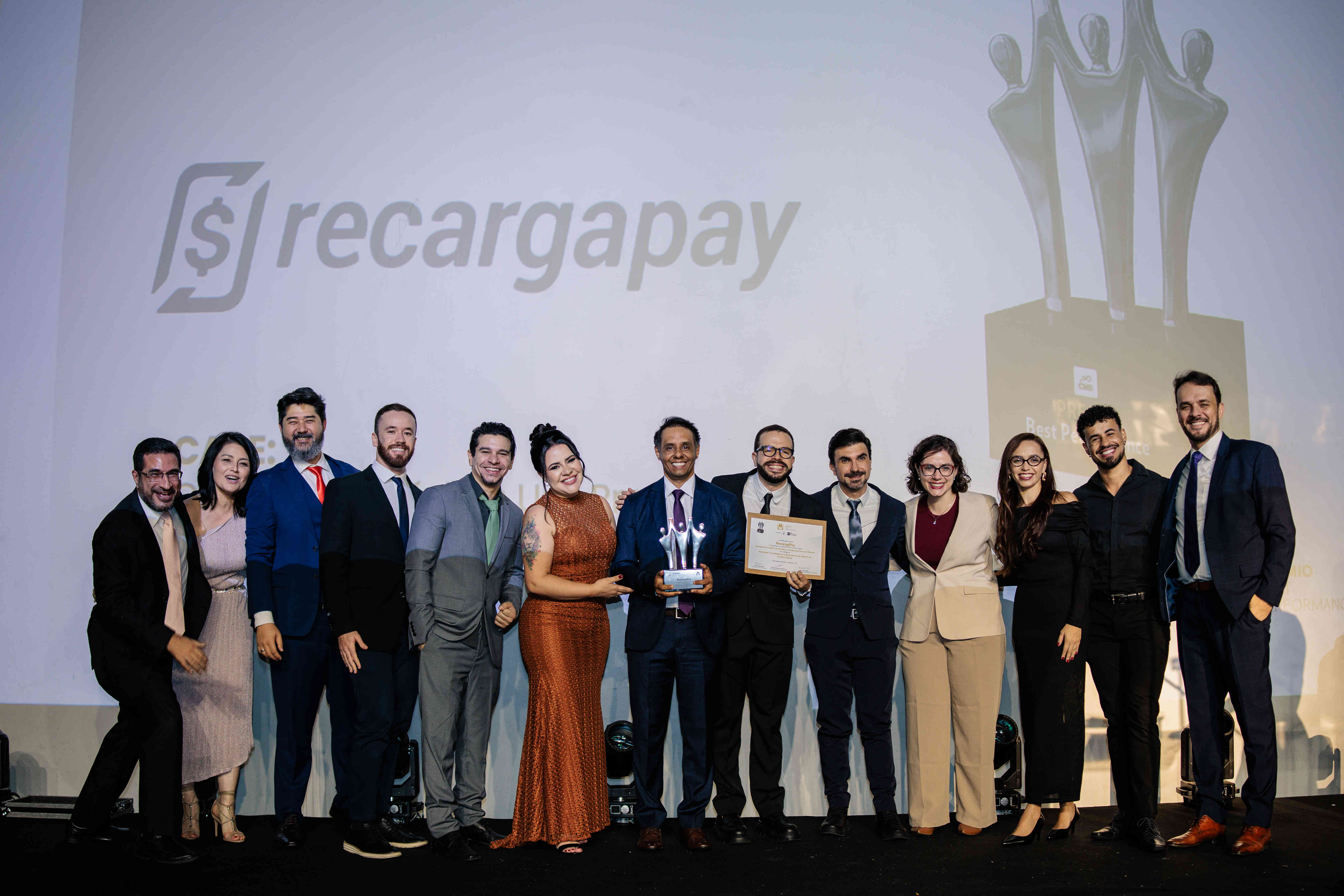 Executivos da RecargaPay posando com troféu prata e certificado no palco do Prêmio Best Performance 2025