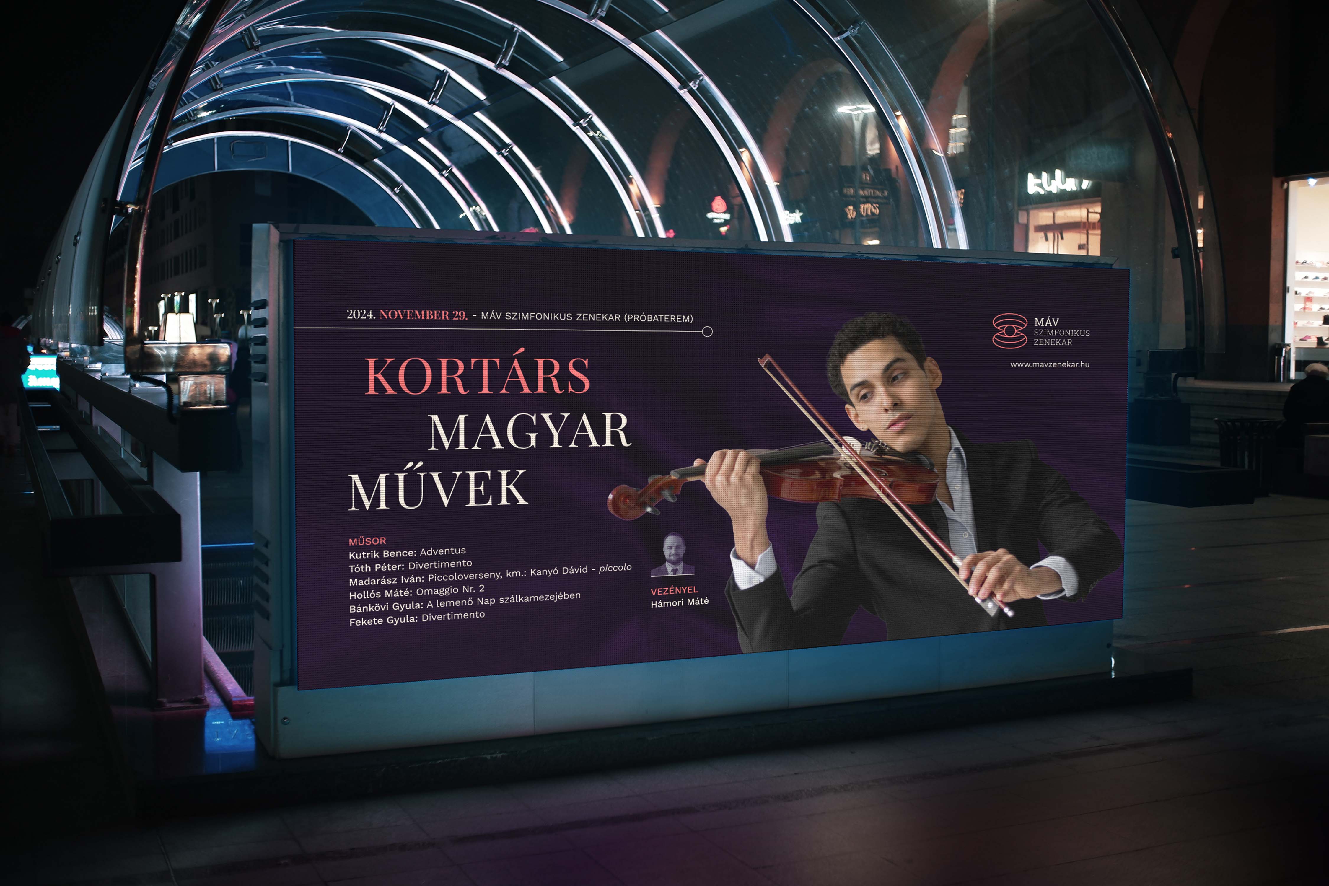 Large illuminated billboard at a metro entrance promoting the concert with V1 logo and violin soloist - MÁV Symphony Orchestra, a symphony orchestra brand identity.