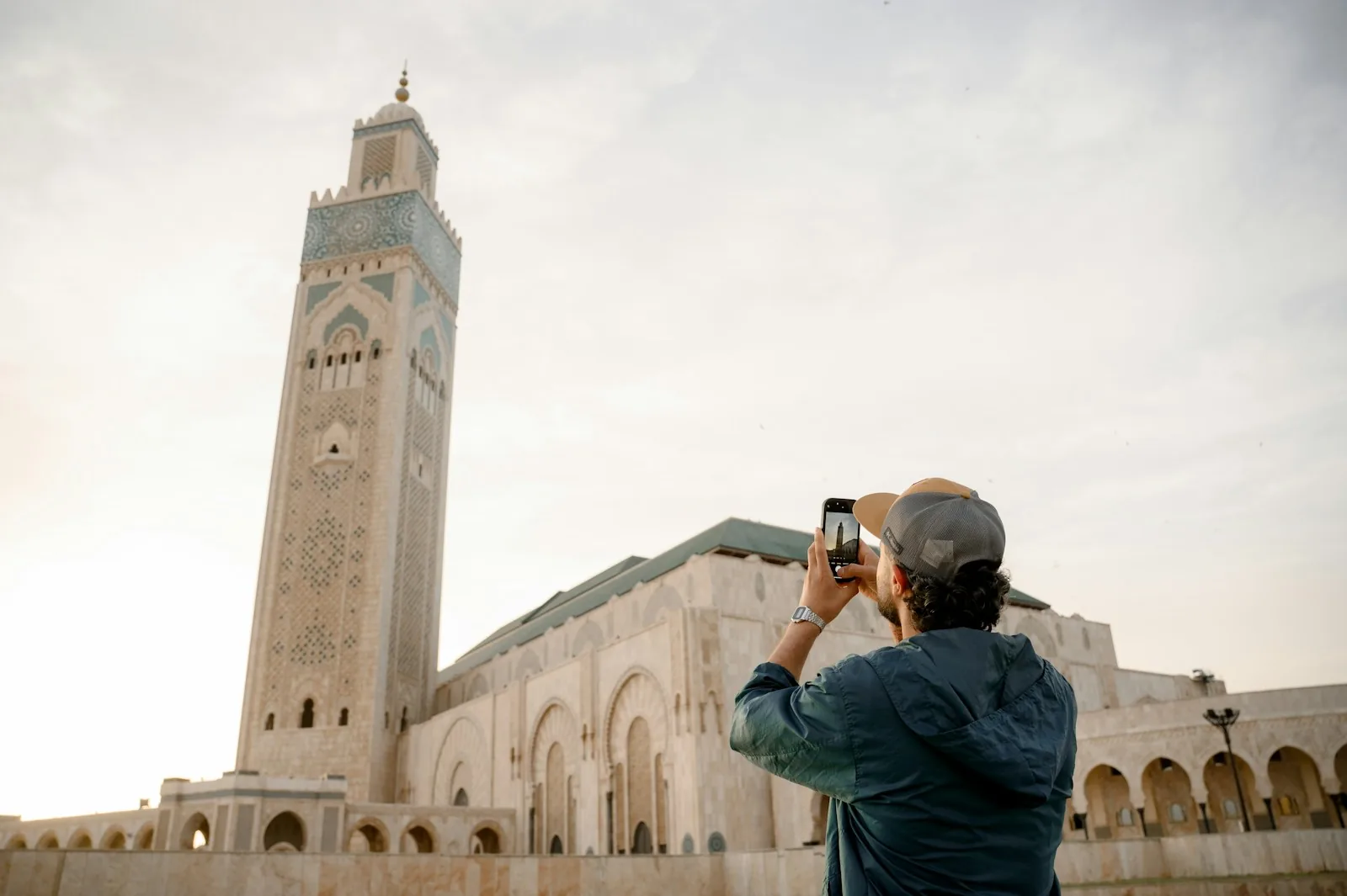 Man in a cap photographing the minaret of the Hassan II Mosque in Casablanca with his smartphone