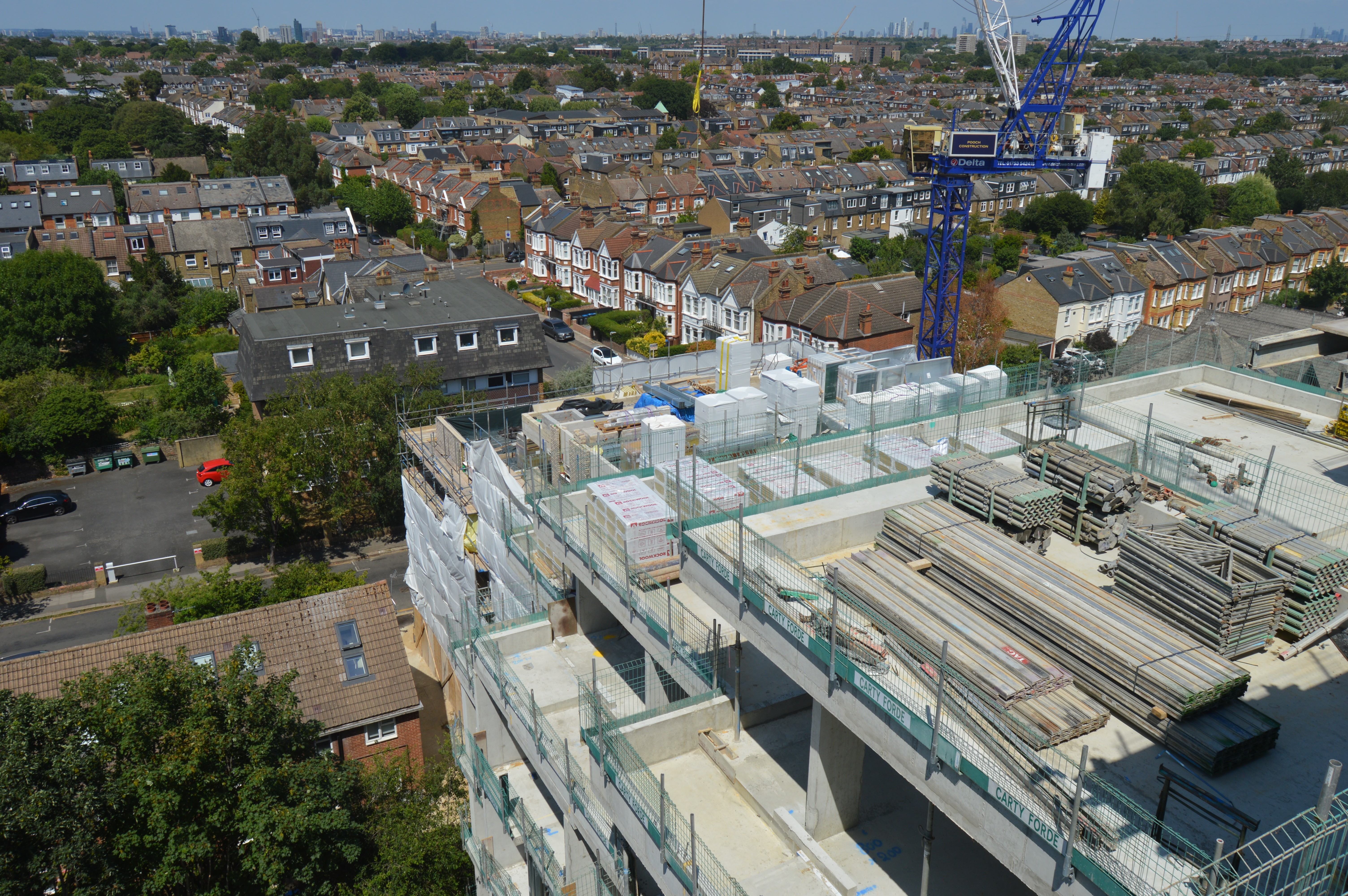 An aerial shot of a modern building under construction with construction materials and a tower crane visible 