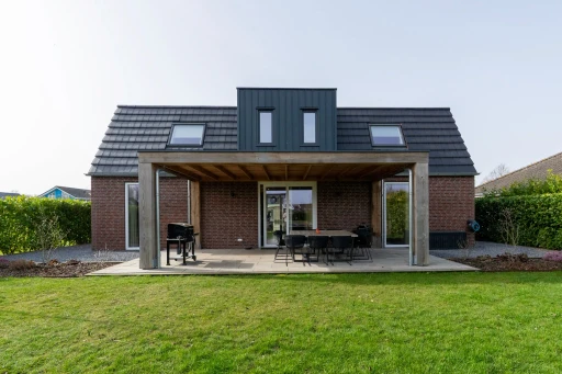 De achterzijde van de vakantiewoning met een overdekte veranda en een ruim gazon.