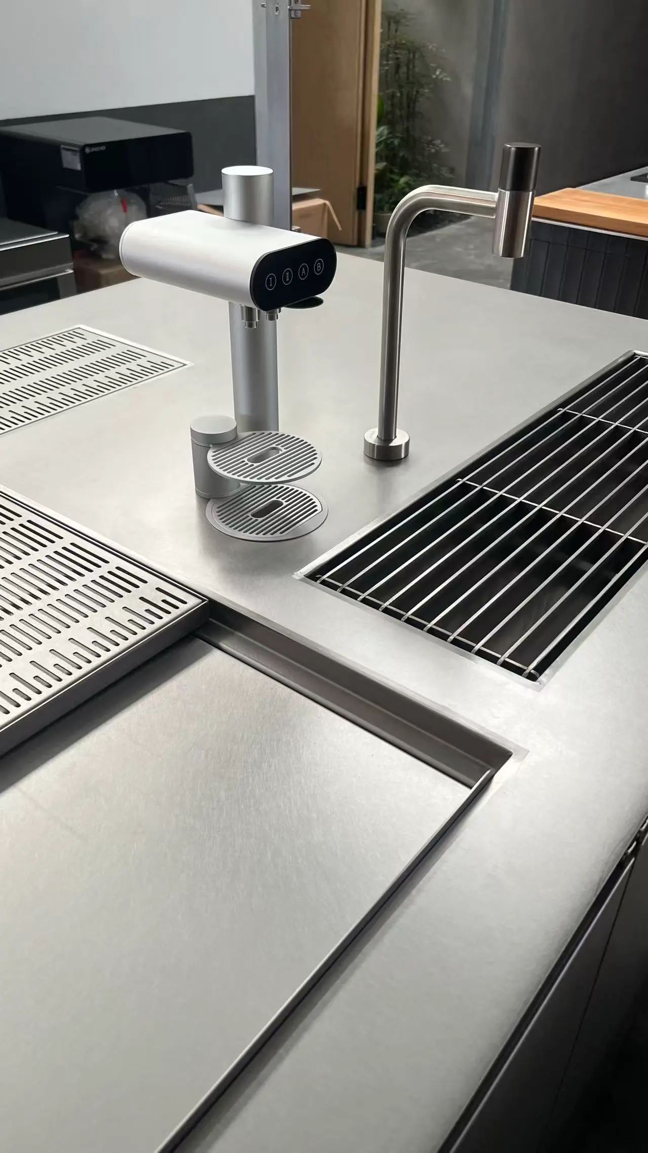 A stainless steel commercial bar and coffee station setup.&nbsp;   Details: Features a brushed metal countertop with integrated drainage grates, a multi-button dispensing tower with dual small drip trays, and a curved faucet.&nbsp;