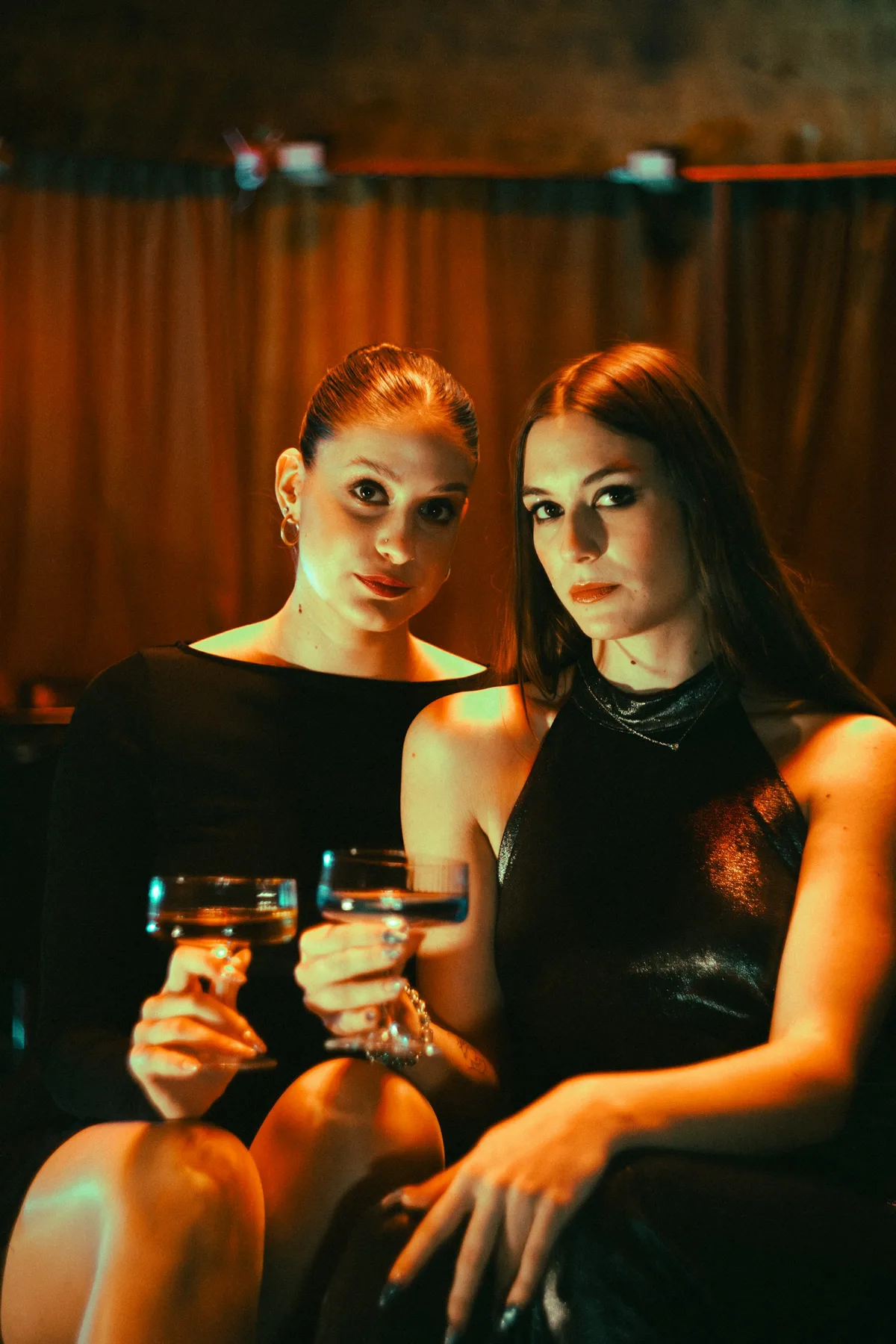 Two women in black dresses holding drinks at a ladies night in a Dubai lounge