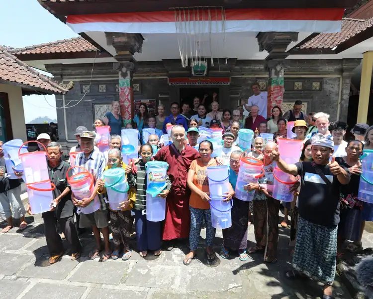 Balinese villagers and elders hold water filters in front of a traditional temple during a community distribution day.