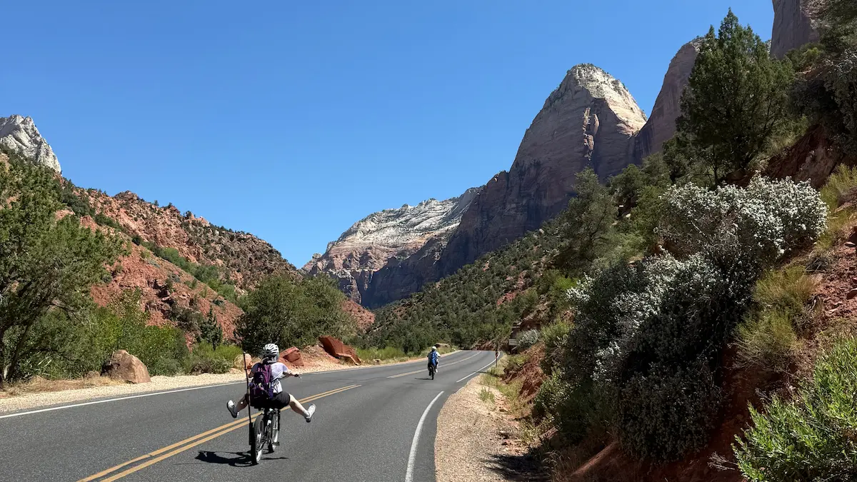 Stu and family riding bikes down a winding mountain road in Zion National Park—capturing motion, freedom, and the journey of living one mile at a time.