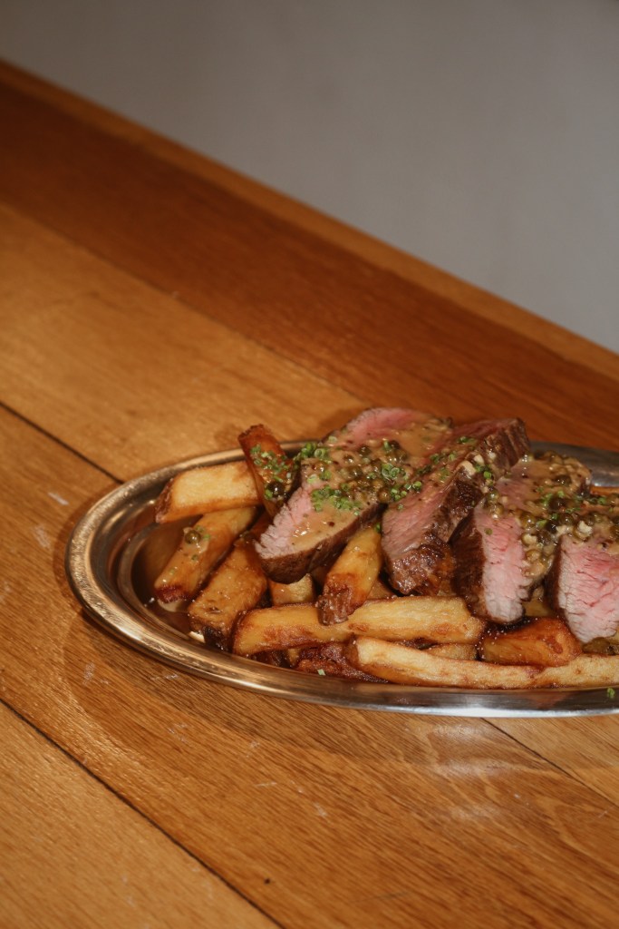 A plate of sliced beef with a savory sauce, served alongside golden fries, arranged on a metal platter against a wooden table.