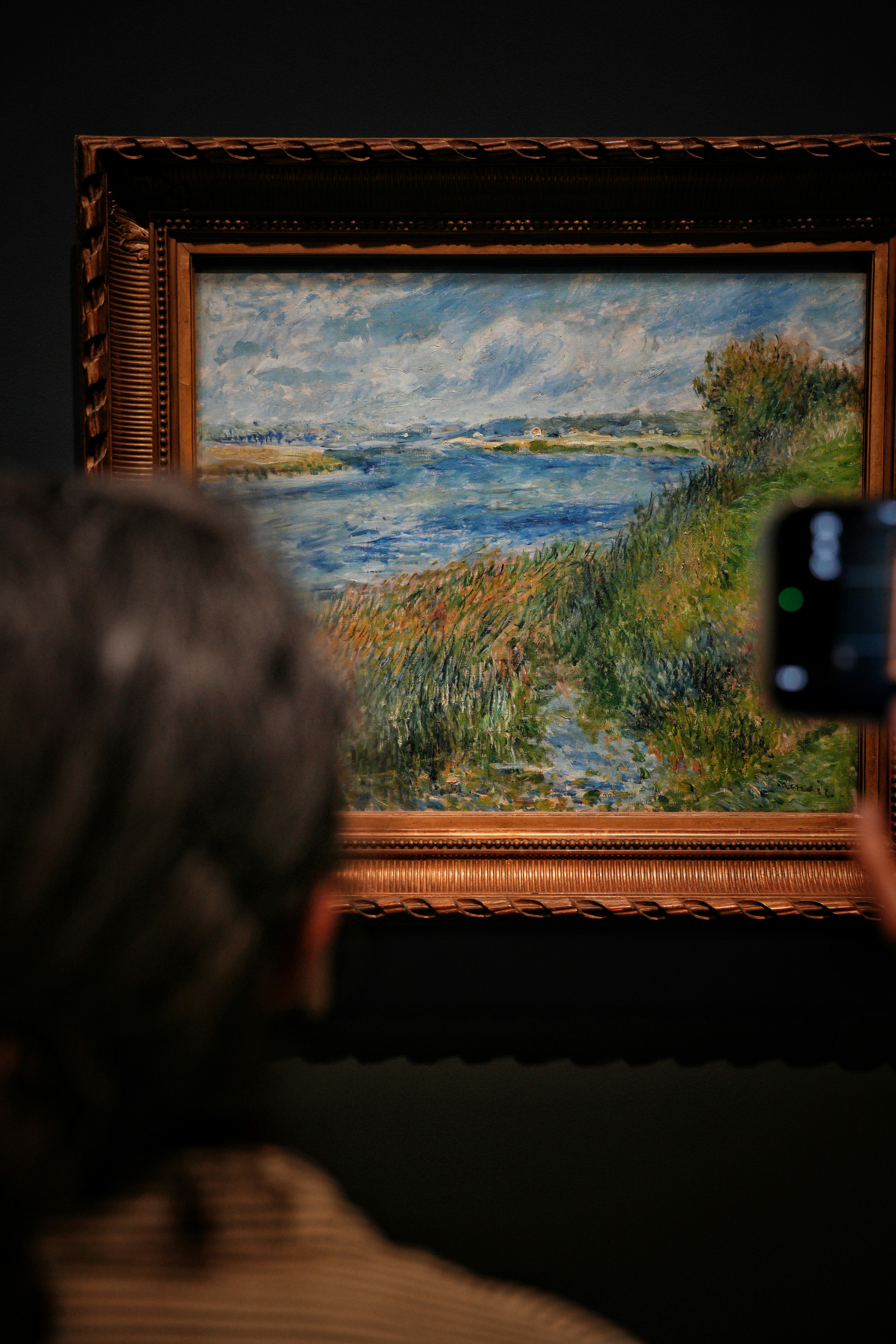 Person photographing a painting of a river landscape
