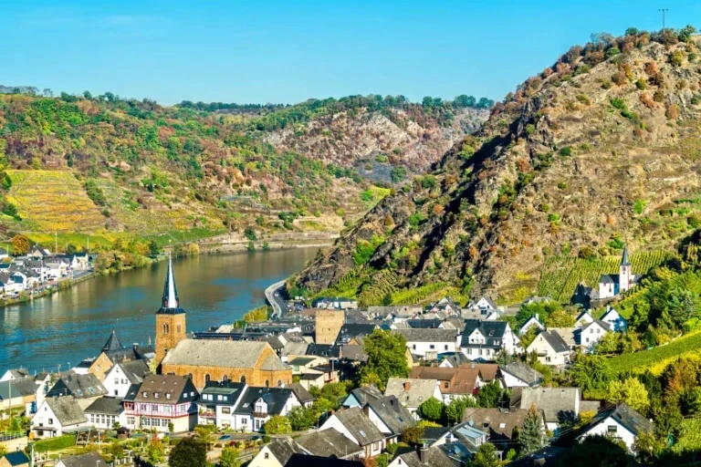 Ein malerischer Blick auf ein Flusstal mit üppigen Hügeln, einem idyllischen Dorf und einer Kirche, eingebettet in die Landschaft.