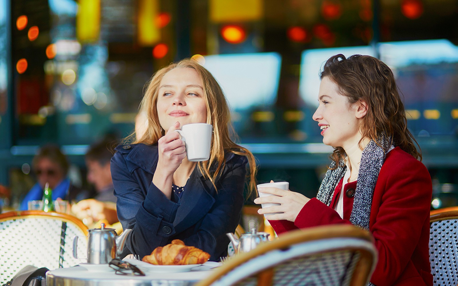 Duas jovens garotas aproveitando um café em uma mesa de cafeteria com croissants.