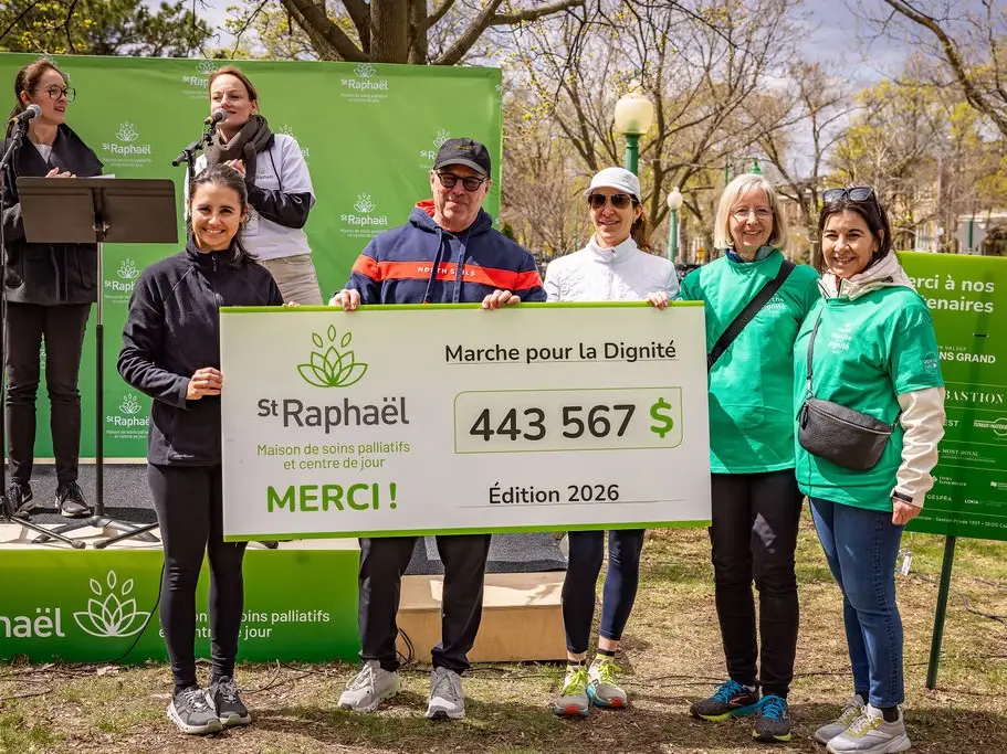 Thought process Thought process EN: Participants and organizers present a ceremonial cheque for $443,567 raised at the 2026 Marche pour la Dignité in support of Maison de soins palliatifs St Raphaël, with Valsoft listed among the partners on the banner.