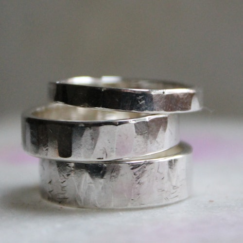 三个叠放在一起的银戒指，带有锤击纹理，置于中性色背景上。