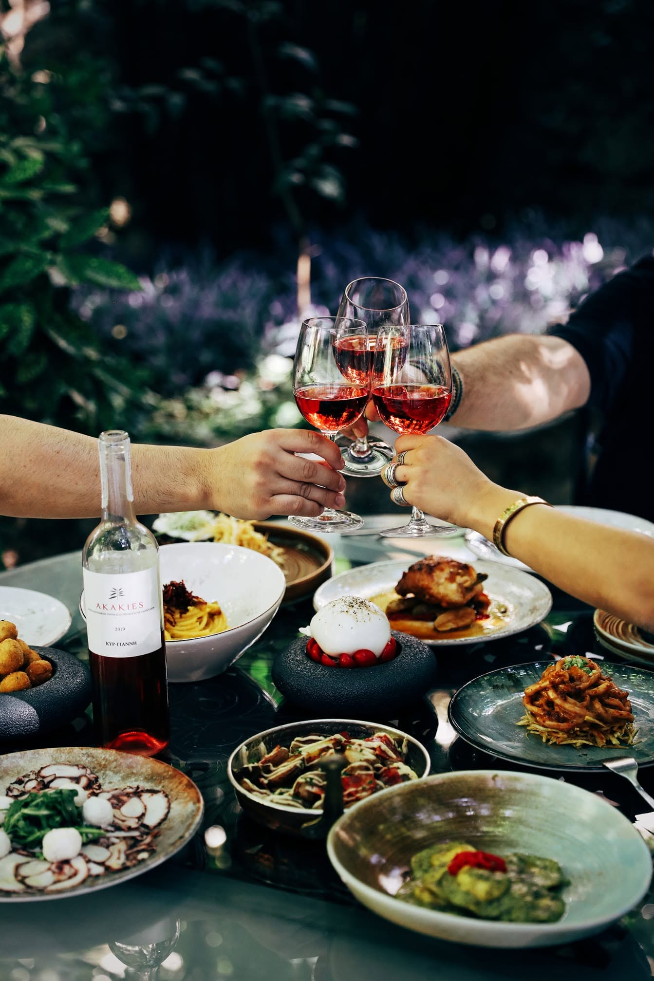 Friends toasting rose over Greek dishes at Palea Poli boutique hotel, Naousa old town