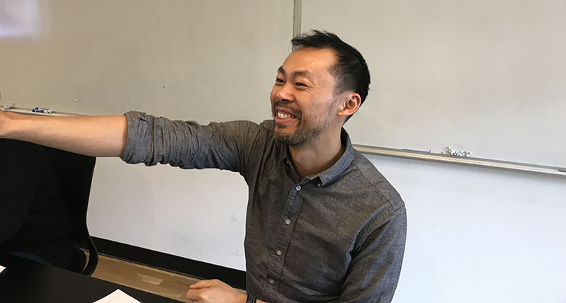 A photo of a smiling man sitting at a desk.