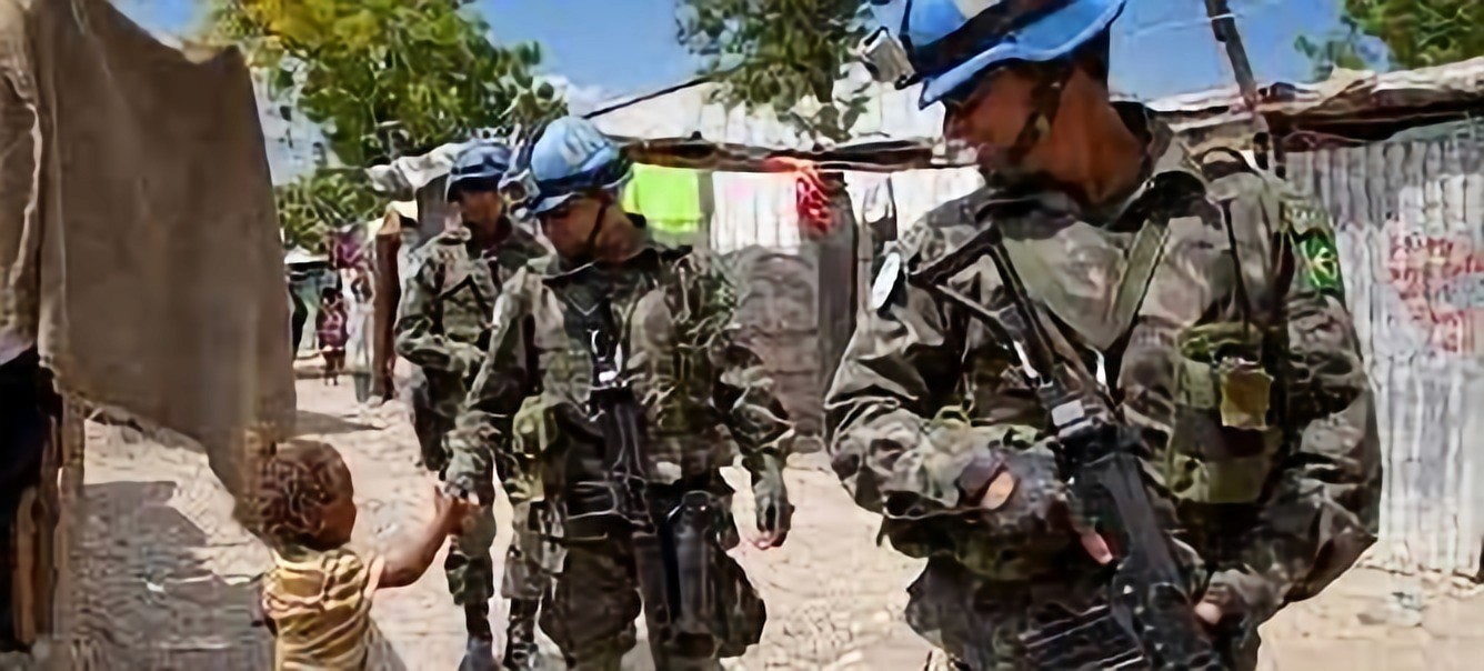 Three United Nations Peacekeepers pass a young Haitian boy. The middle peacekeeper is touching the boy's hand.