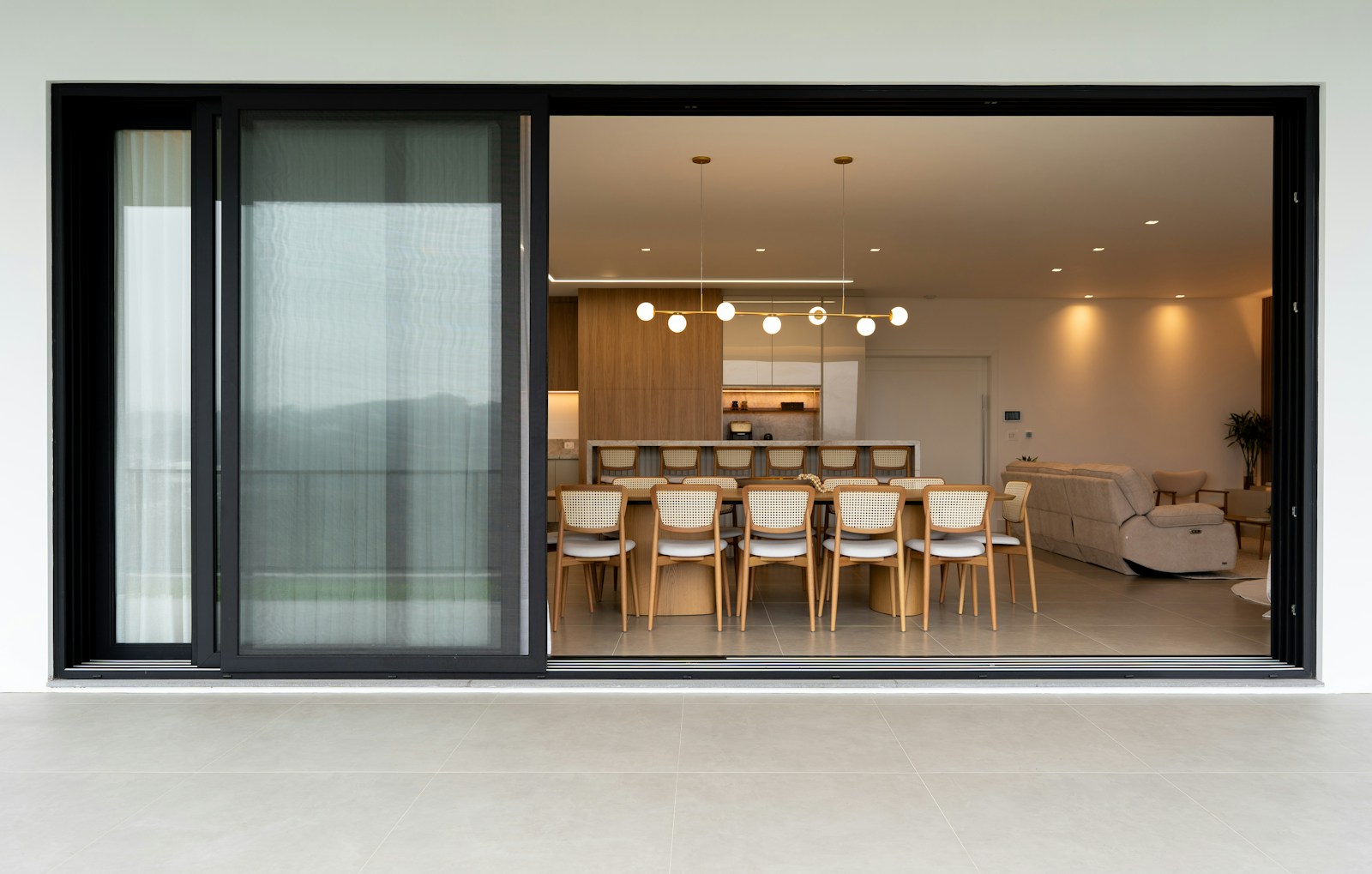 A kitchen and dining room seen through a wide sliding door at dusk