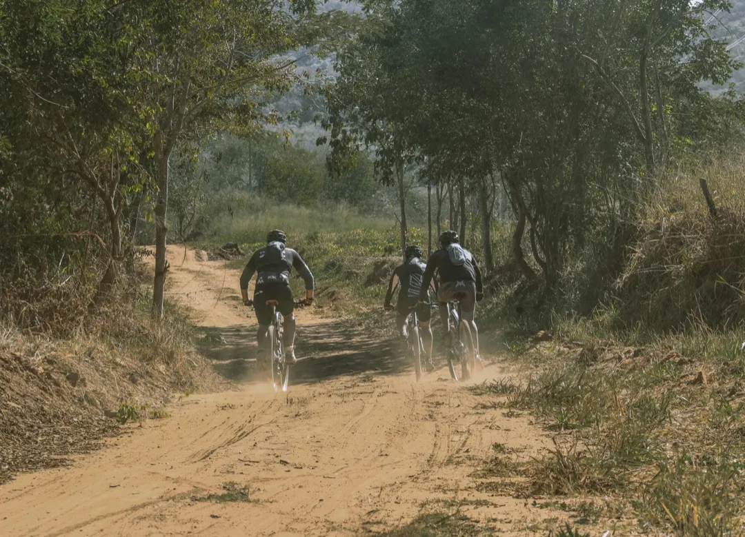 three mountain bikers ride down a dusty track