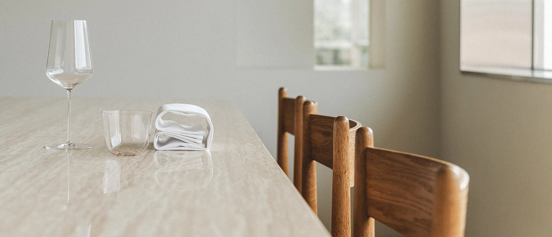대리석 테이블 위에 와인잔과 유리컵, 접힌 냅킨이 놓인 미니멀한 실내 공간