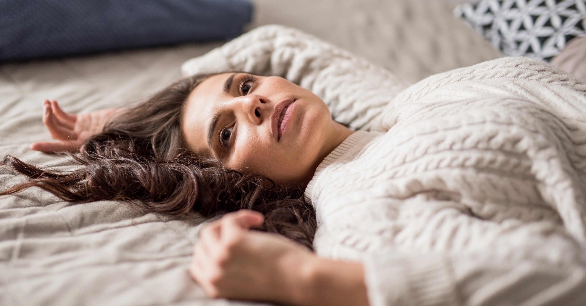 En kvinna ligger på sängen och tittar med en tom blick upp på taket.
