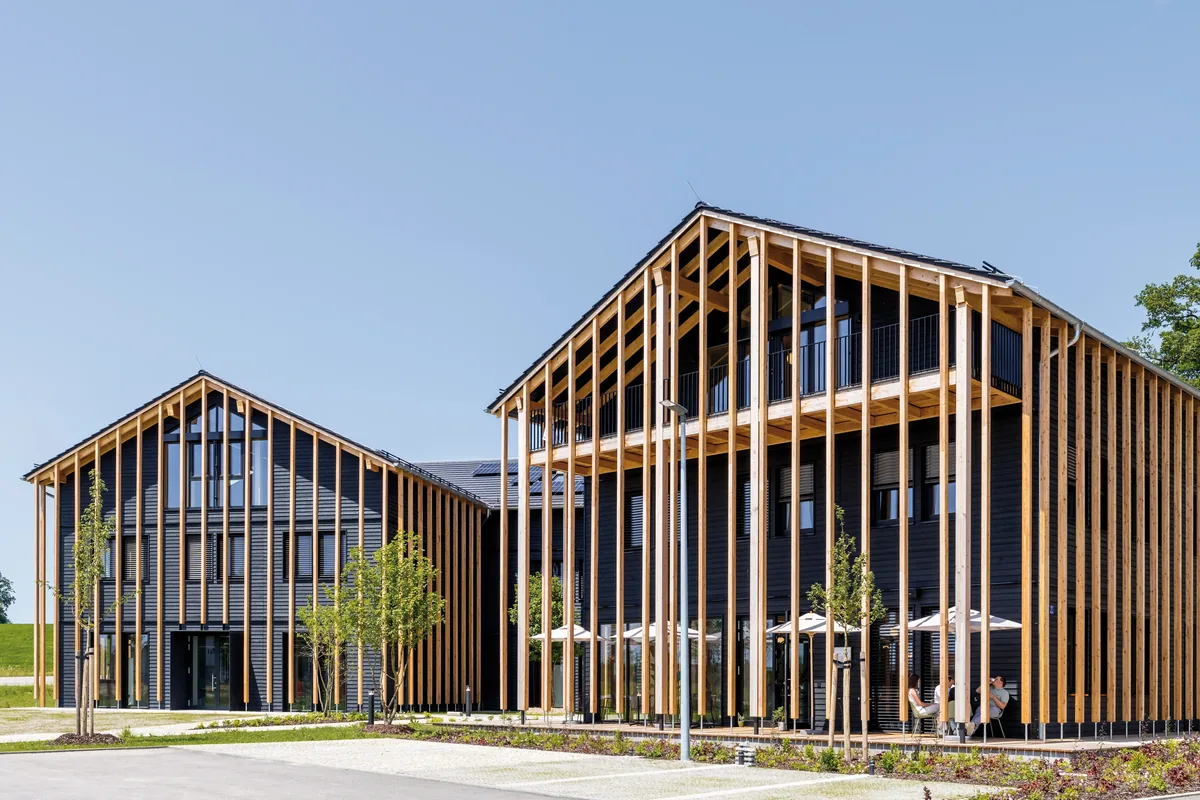 Modern wooden building with large windows and vertical beams under blue sky.